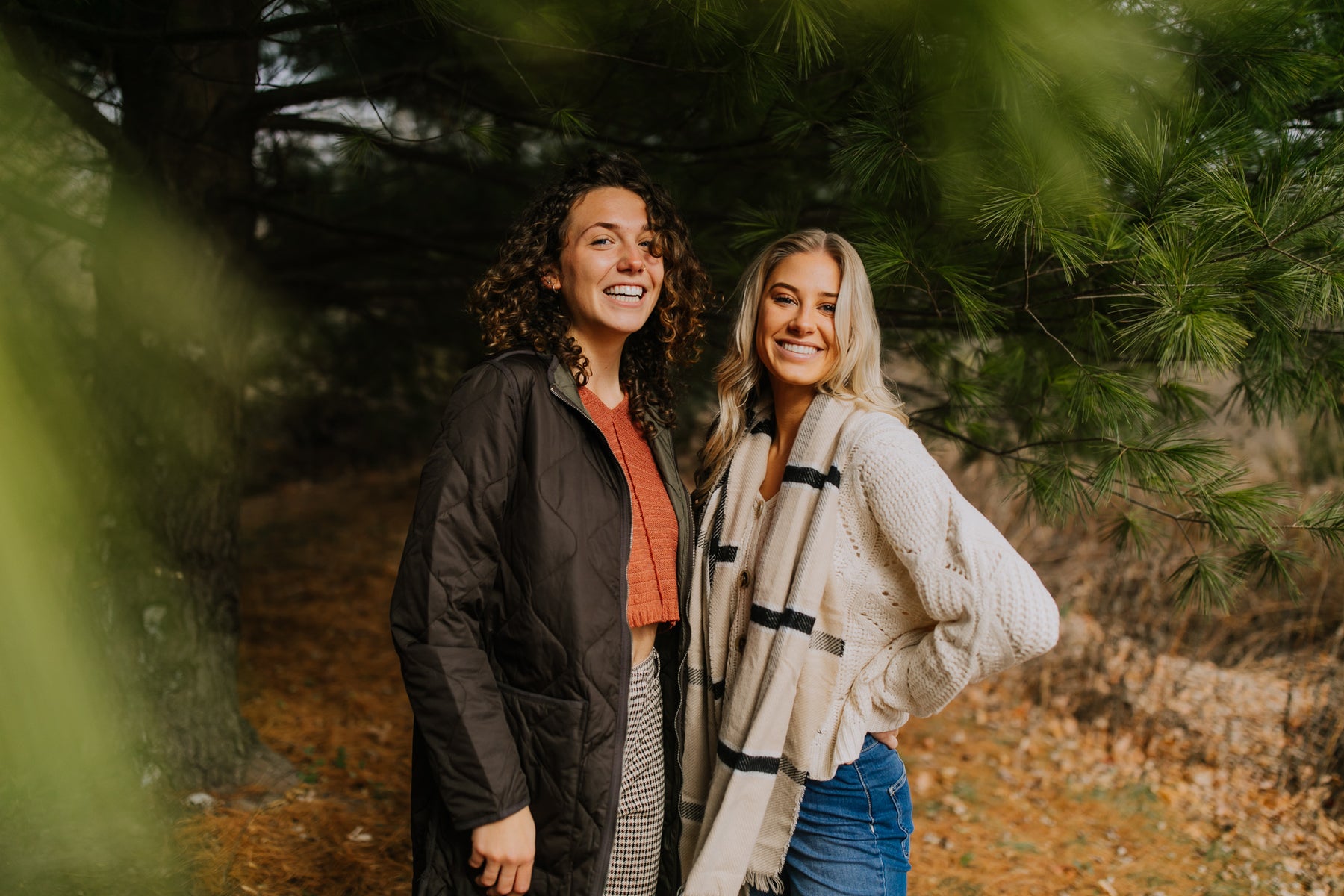 two women standing under some pine trees